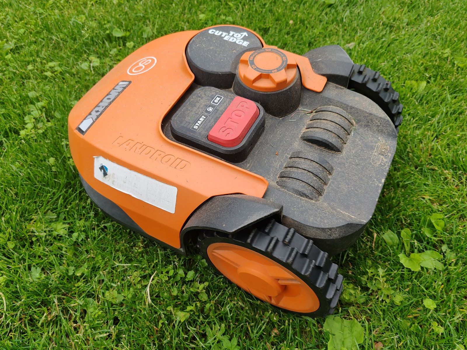 Orangefarbener Mähroboter auf einem grünen Rasen